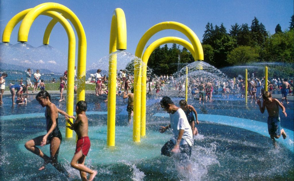 Bright yellow tubes shoot out water as young children run around in the water.