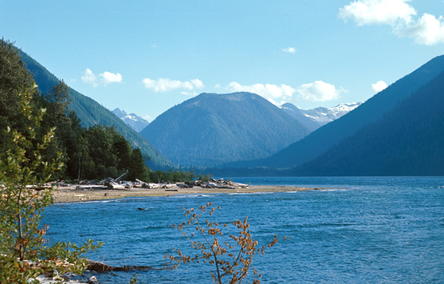 A beautiful photo of a sandy beach on a blue sky day with mountains in the background.