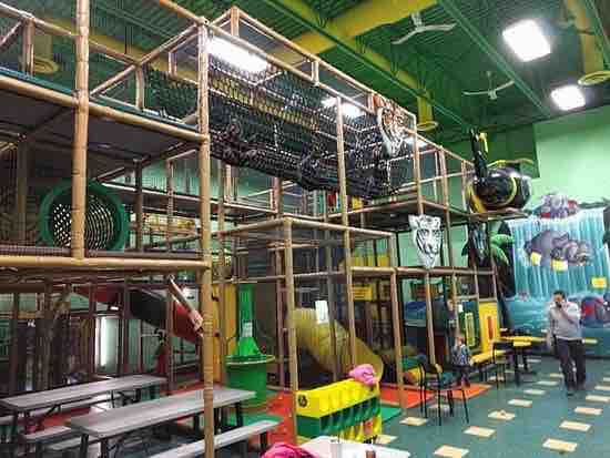 A child stands outside of a big play structure while a dad looks on talking on his cellphone at Go Bananas.