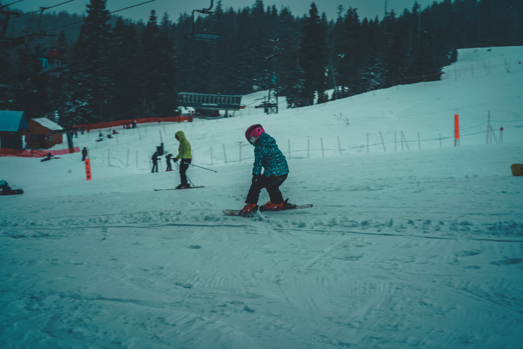 Young kids are wearing skis on the bunny hill slope.