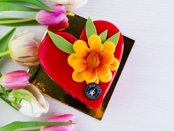 A read heart shaped cakes decorated with an edible yellow flower on top.