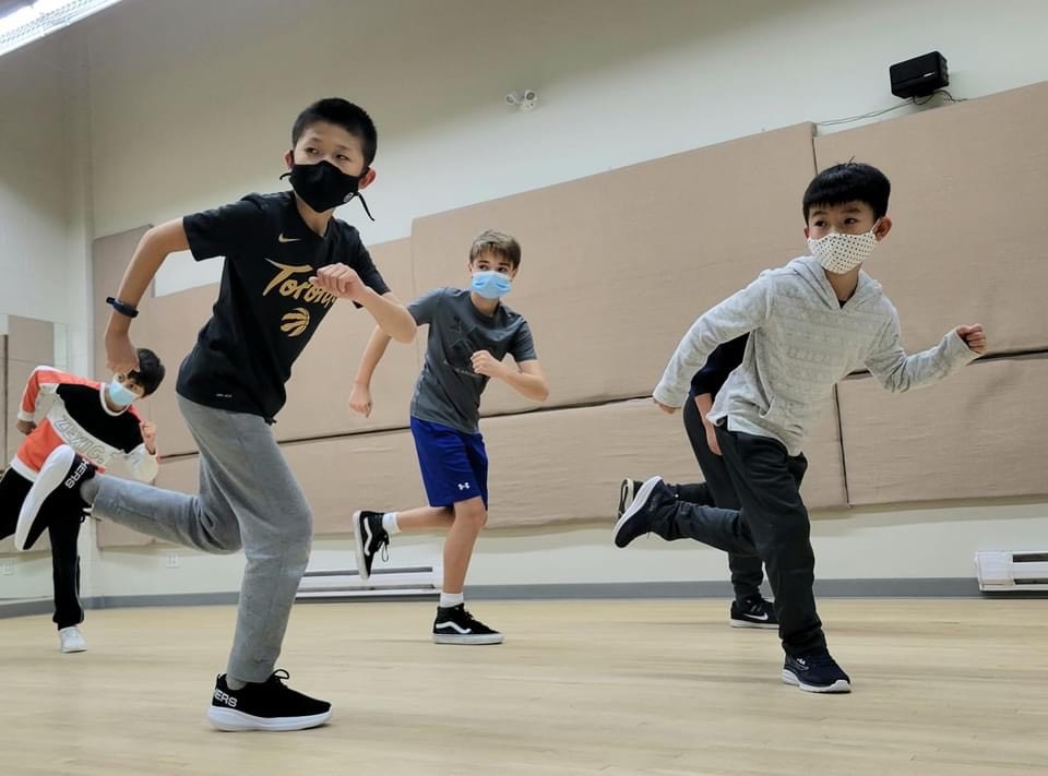 Four boys pose like they are doing a running dance. They look to the left of the camera.