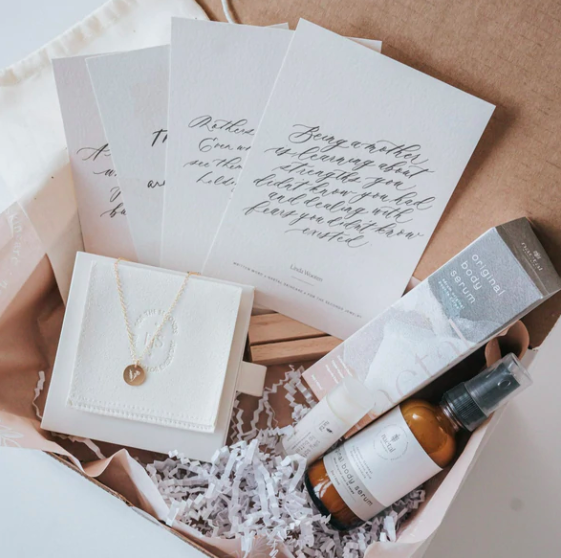 A top view basket of cards, room spray and a necklace with a v on it..