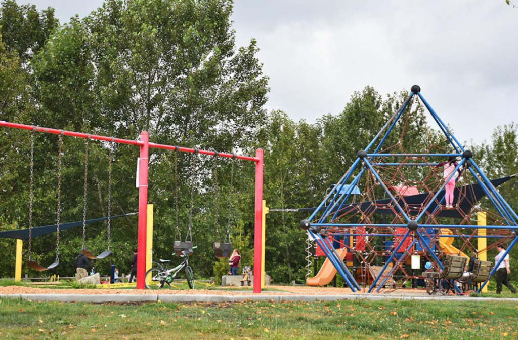 A playground red, blue, and yellow structor with three slides and various climbing fixtures. A set of swings are in the foreground.