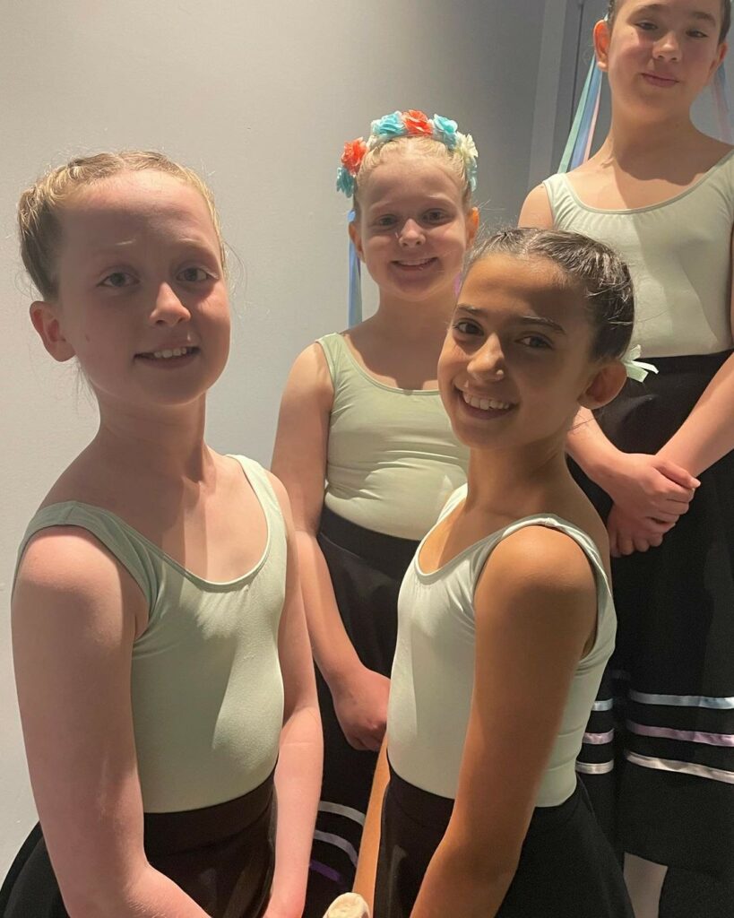 Four young girls smile into the camera wearing light green tops and black skirts.