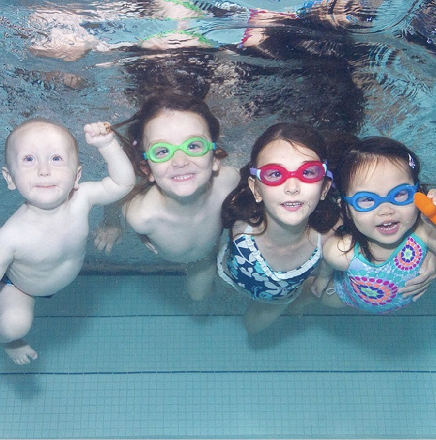 Three children and one baby are fully submerged under water. They all smile at the camera.