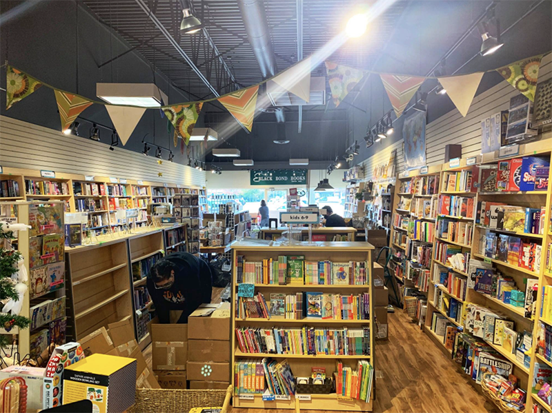 A picture from the back wall of a bookshop showing wall to wall books and colourful bunting hanging from the ceiling.