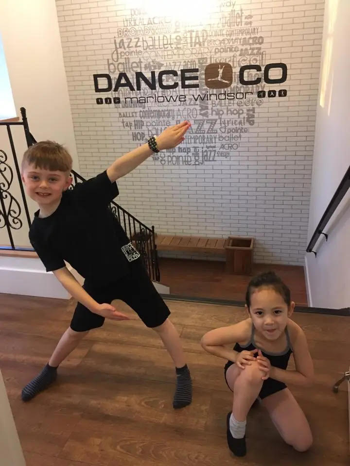 A young boy and girl pose in front of a brick wall with Dance Co printed on the wall.