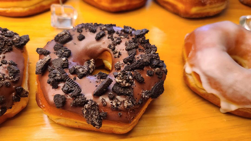 A close up of a donut with chocolate icing and Oreo crumbs.