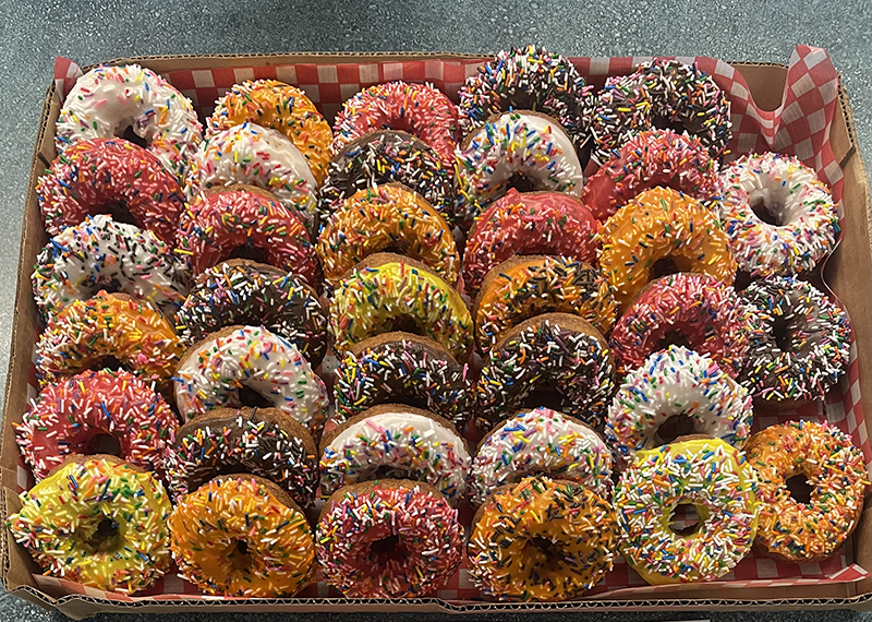 A basket of several donuts all iced and covered in sprinkles in various colors.