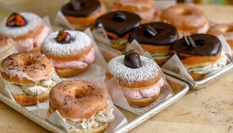 A trey of 4 rows of donuts is taken at an angle. The donuts all of cream filling.