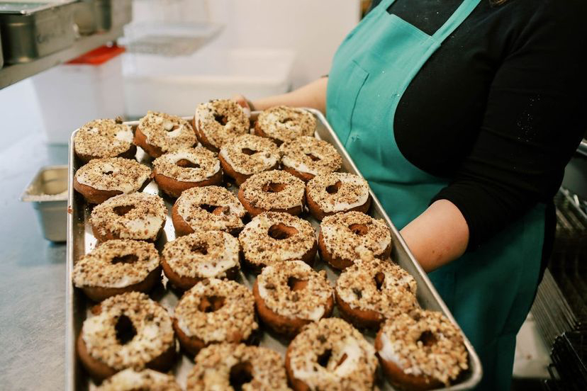 A woman holds a very large tray of iced donuts.
