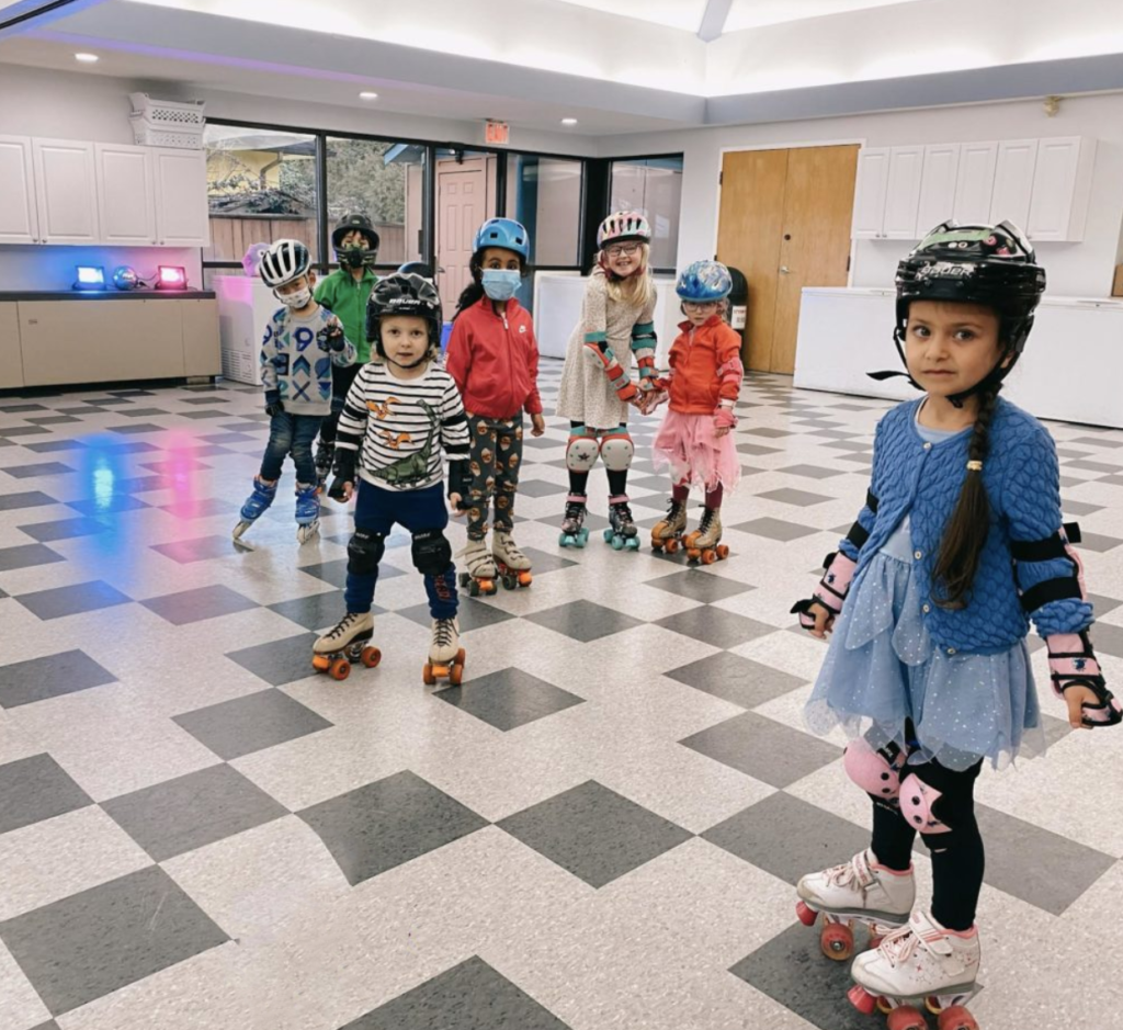 A photo of a group of small children dressed in roller skate safety gear all the kids are looking at the camera.