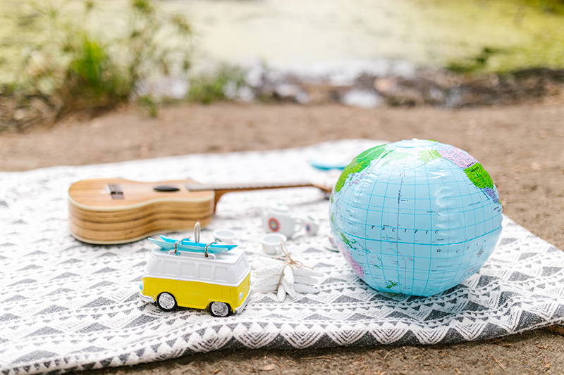 A photo of a picnic blanket with a small toy, a world beach ball, and a ukulele sit on the top.