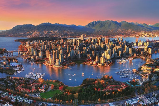 An aerial photo of Victoria Island as the sun is setting. Tall buildings are sprinkled with green trees and grass, surrounded by water that is sprinkled with boats.