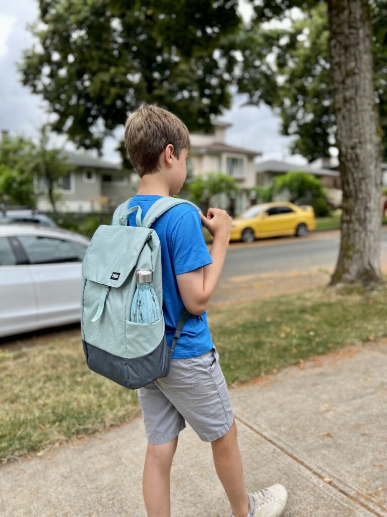 A young boy walks down the street wear in blue Thule Lithos backpack.