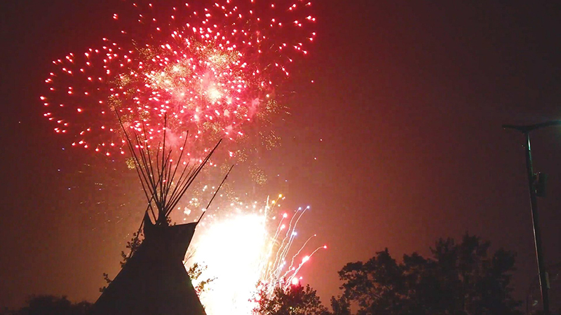 A dark sky is filled with red and orange fireworks with a teepee silhouette.