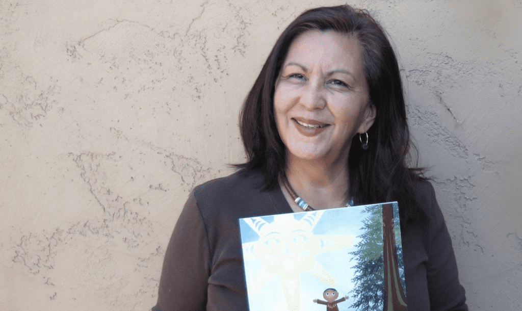 A photo of author Lisa lewis smiling holding her book Tsunaxen's Journey.