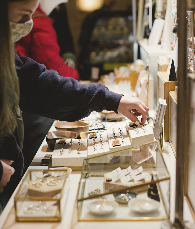 A woman leans over a jewelry booth at a craft fair.