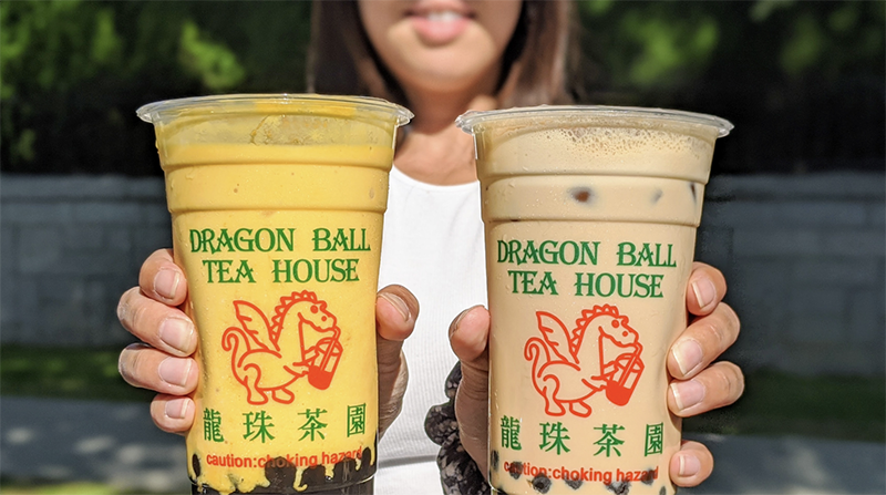 A woman holds two cups of bubble tea in each hand. One is orange and the other light brown, they read Dragon Ball Tea House
