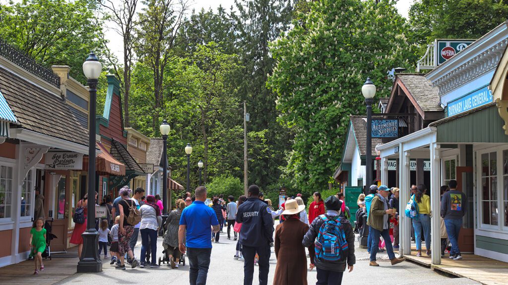 A crowd of people at the Burnaby Village Museum. They are walking around checking out the heritage buildings.