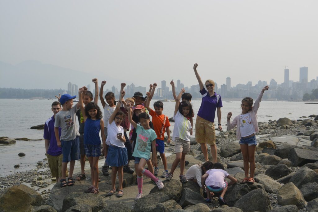 Group of kids from the Pear Tree Education summer camps at the beach raising their hands and having fun