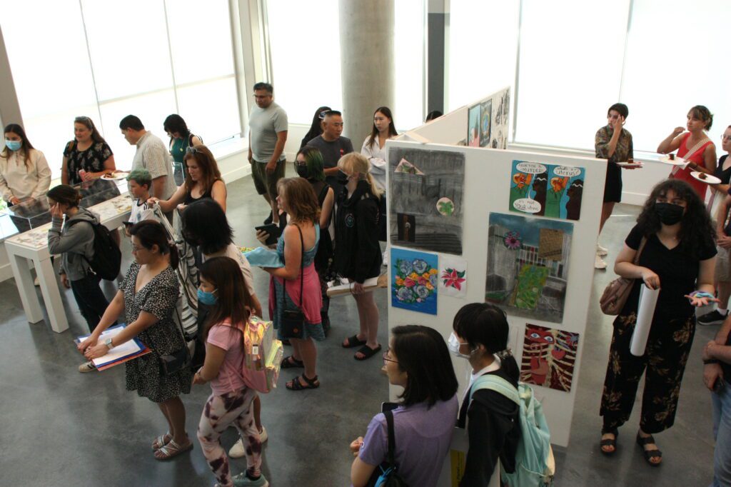 A bunch of people looking at a display of artwork at an exhibition at the Emily Carr University for the Teen Programs