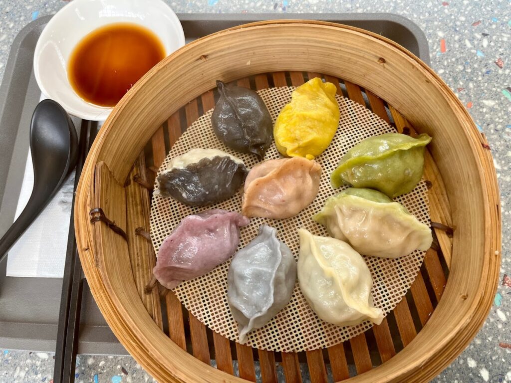 Differrent colours of dumplings in a wooden steamer and dipping sauce on the side