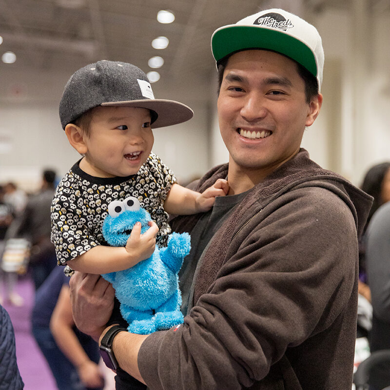 Dad and his baby son smiling, son is holding cookie monster at The Baby Show in Vancouver