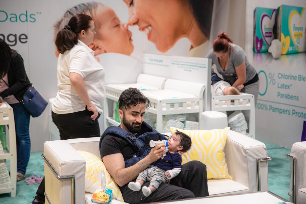 A dad feeding his baby son on a couch in the Pampers area for the Baby Show in Vancouver