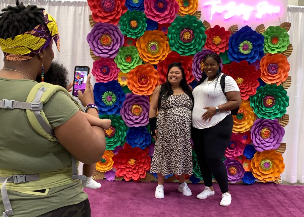 A beautiful colorful flower backdrop for photos. Two pregnant ladies are getting pictures done by another mother at the baby show in Vancouver