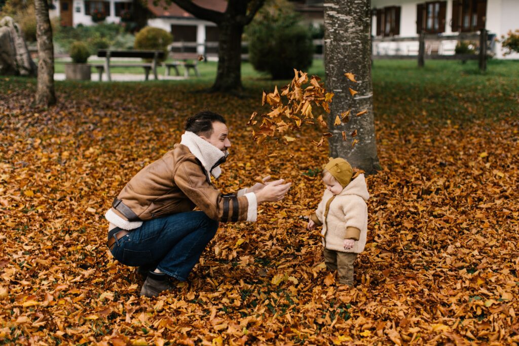 Father in a field of fall leaves with his child throwing leaves in the air for family thanksgiving activities