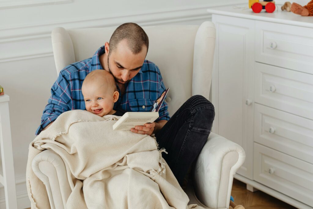 Dad sitting on a rocking chair reading a book to his son as a indoor activity for snow days