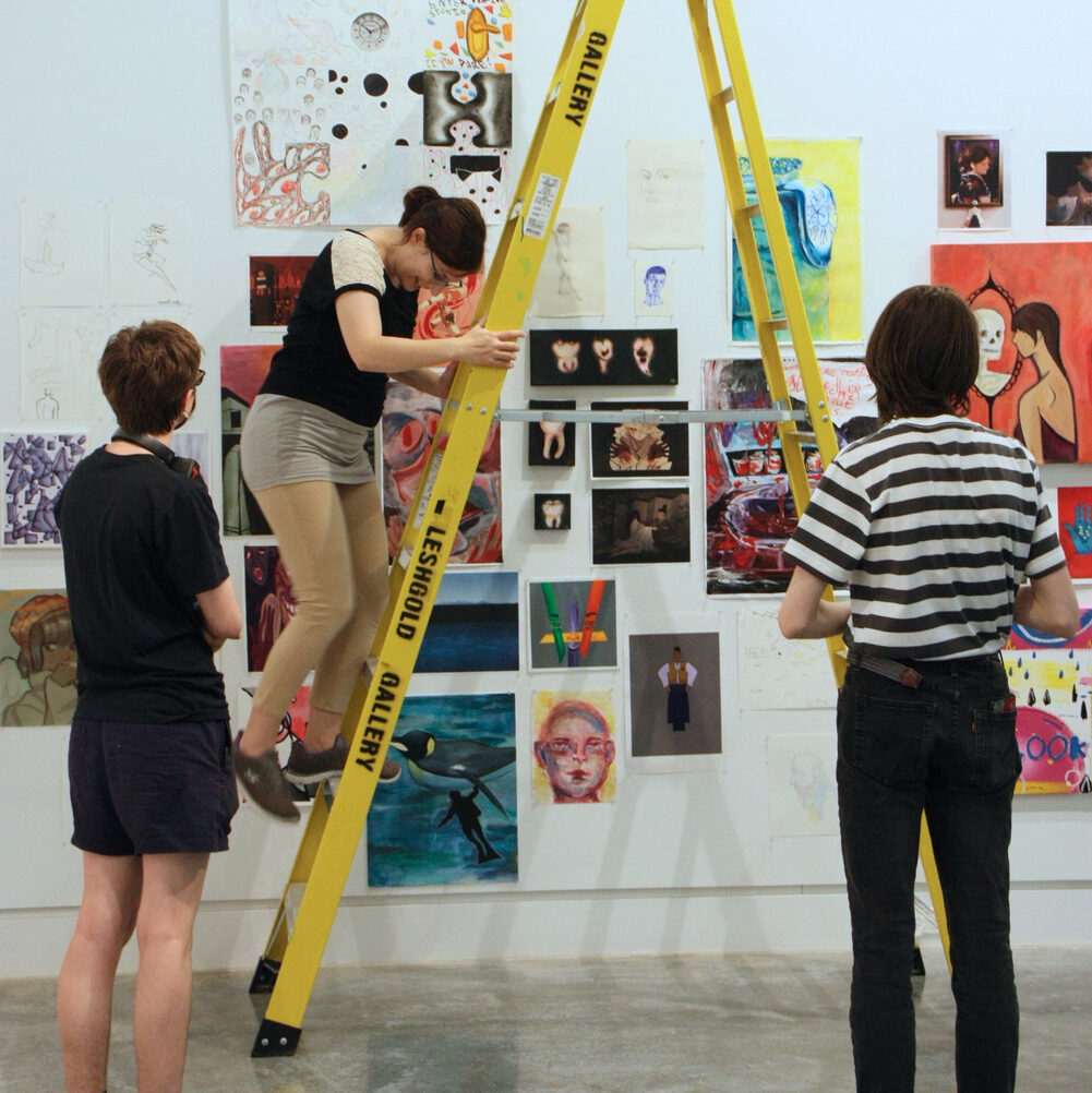 3 ladies admiring and putting the art work of students from the Emily Carr University Summer Camps
