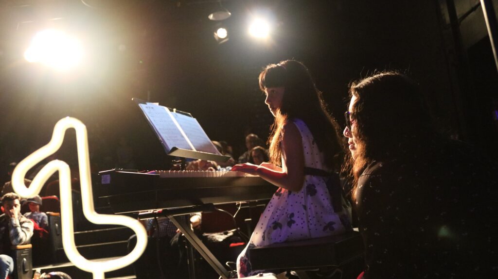 Girl on keyboard in front of an audience by Rockstar Music Central