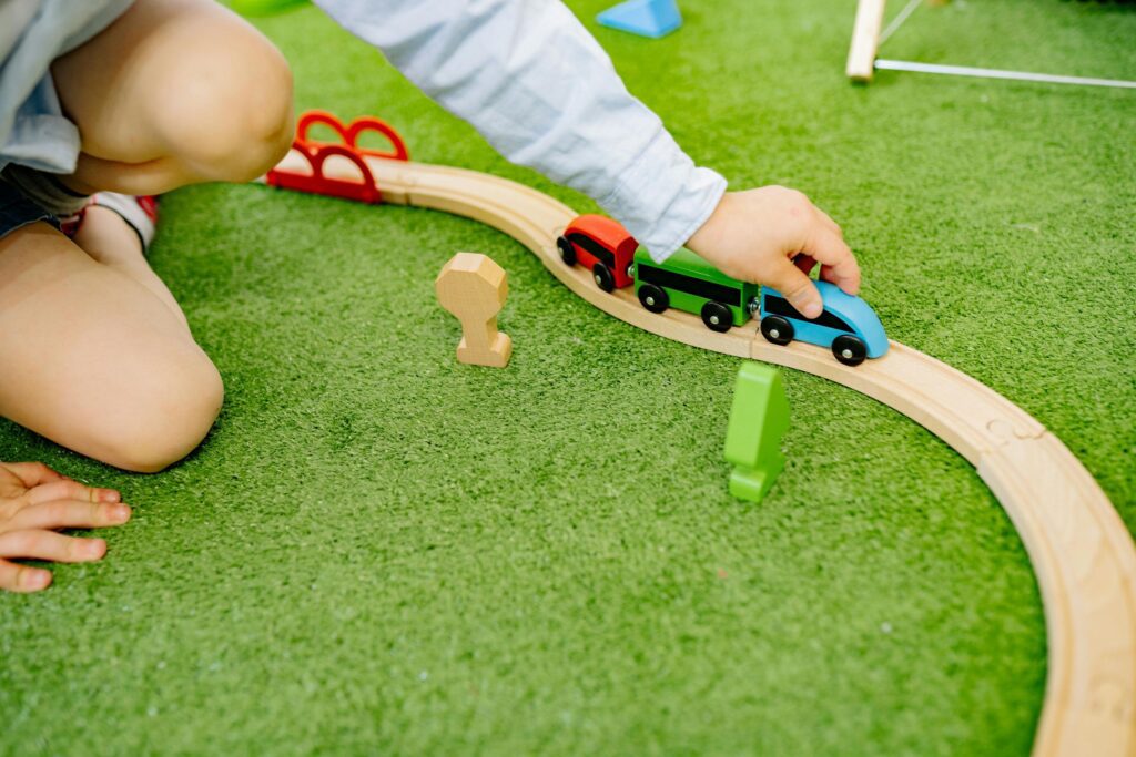Kid playing with trains on a grass turf