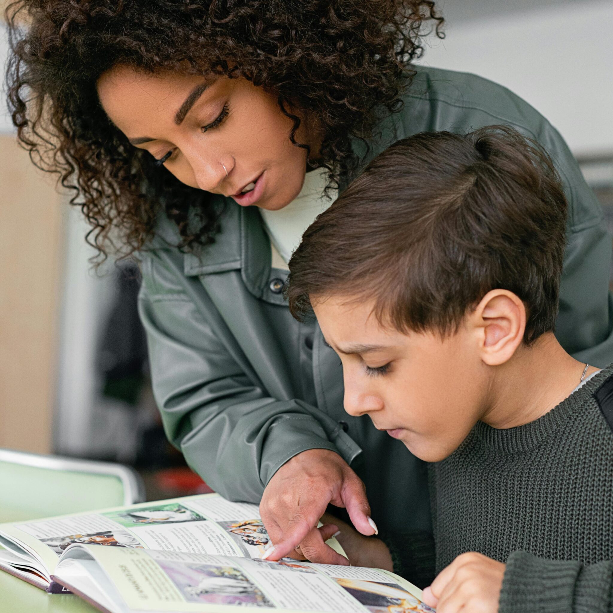 A lady tutor showing a young boy how to read and showing signs of a struggling reader