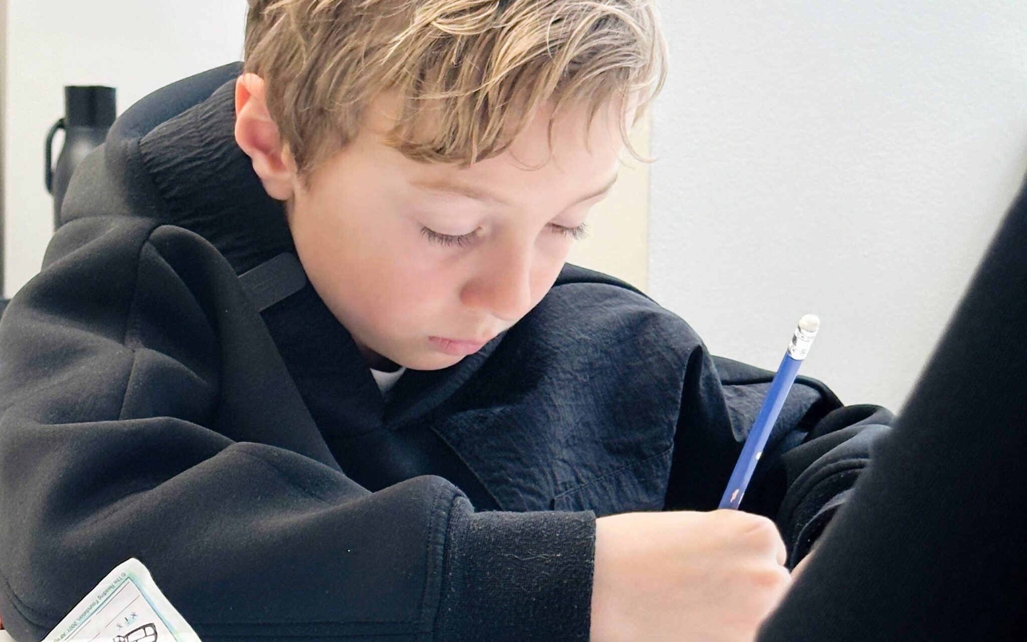 A boy writing on a piece a paper needing help as he has signs of a struggling reader