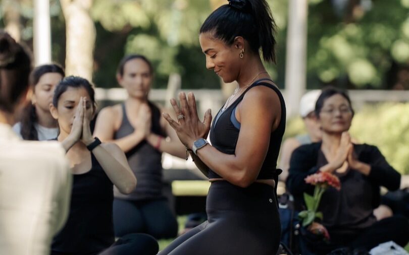 Tara Shayegan doing a Yoga class with a class of women outdoors.