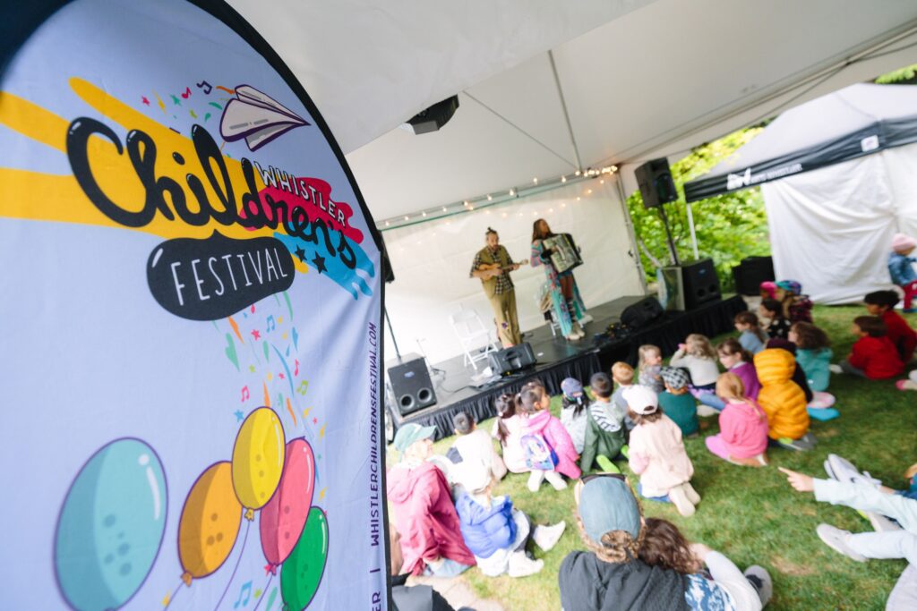 a sign for the Whistler Children's Festival and in the background it's a groups singing to a group of kids