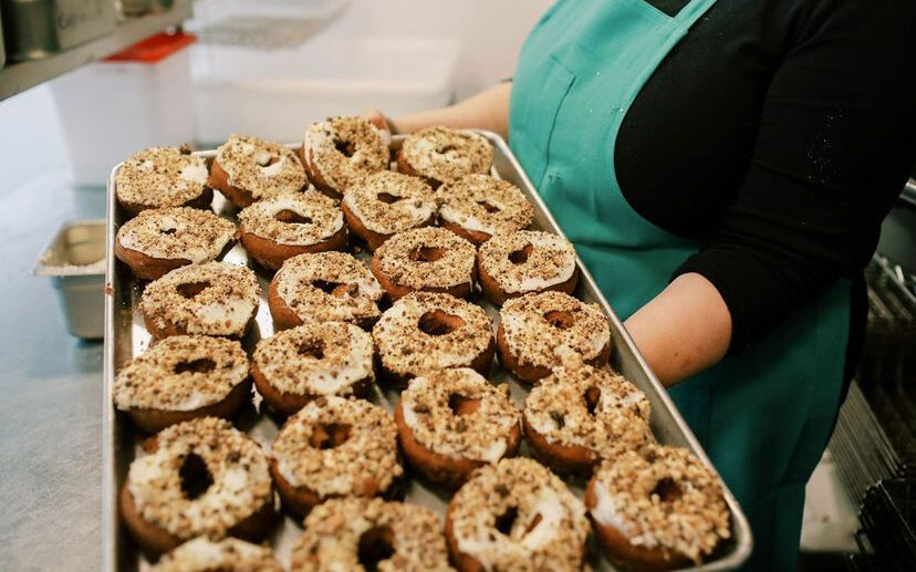A woman holds a very large tray of iced donuts.